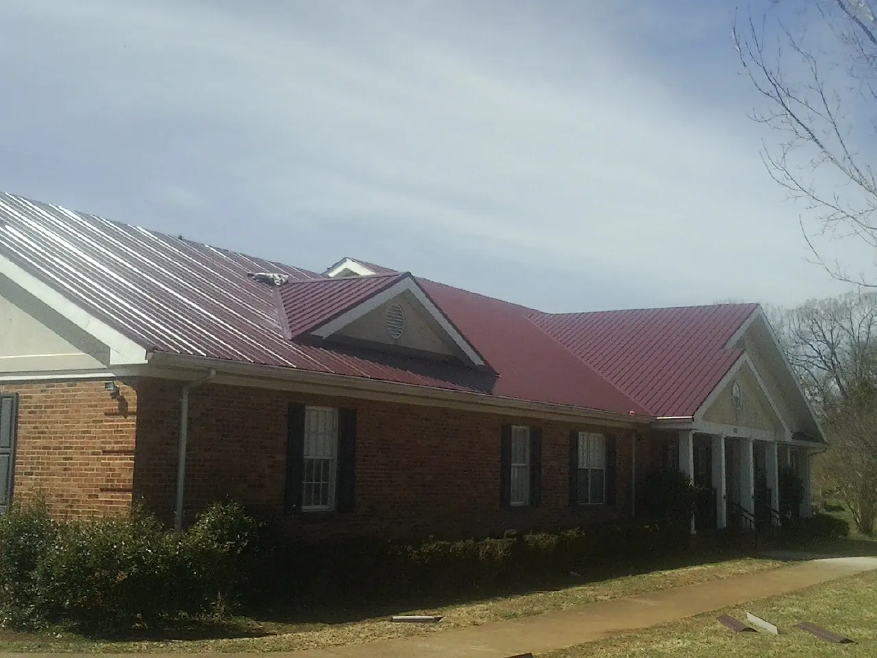 Red metal roof with gabled entries on a long brick building, from a Hail Damage Roof Repair job in Clarkson