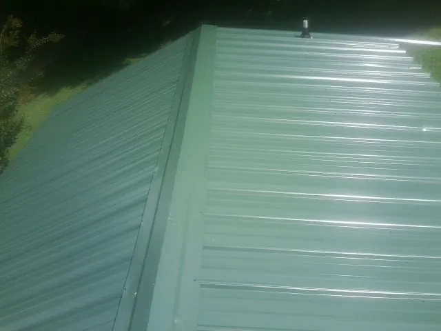 New green metal panels meeting at the ridge of a roof — Flat Roof Repair work by our crew in Clarkson