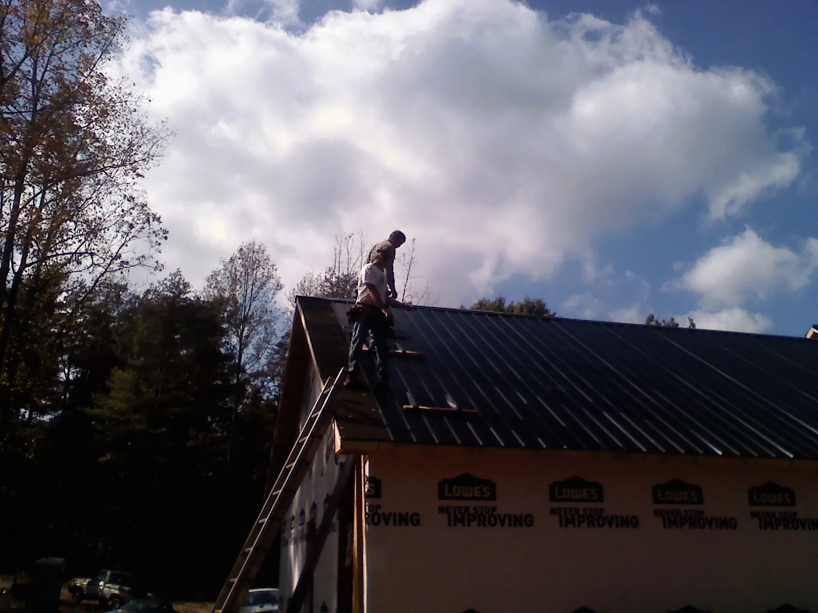 Roofer fastening dark metal panels high against a cloudy sky, from a Roof Inspection job in Clarkson