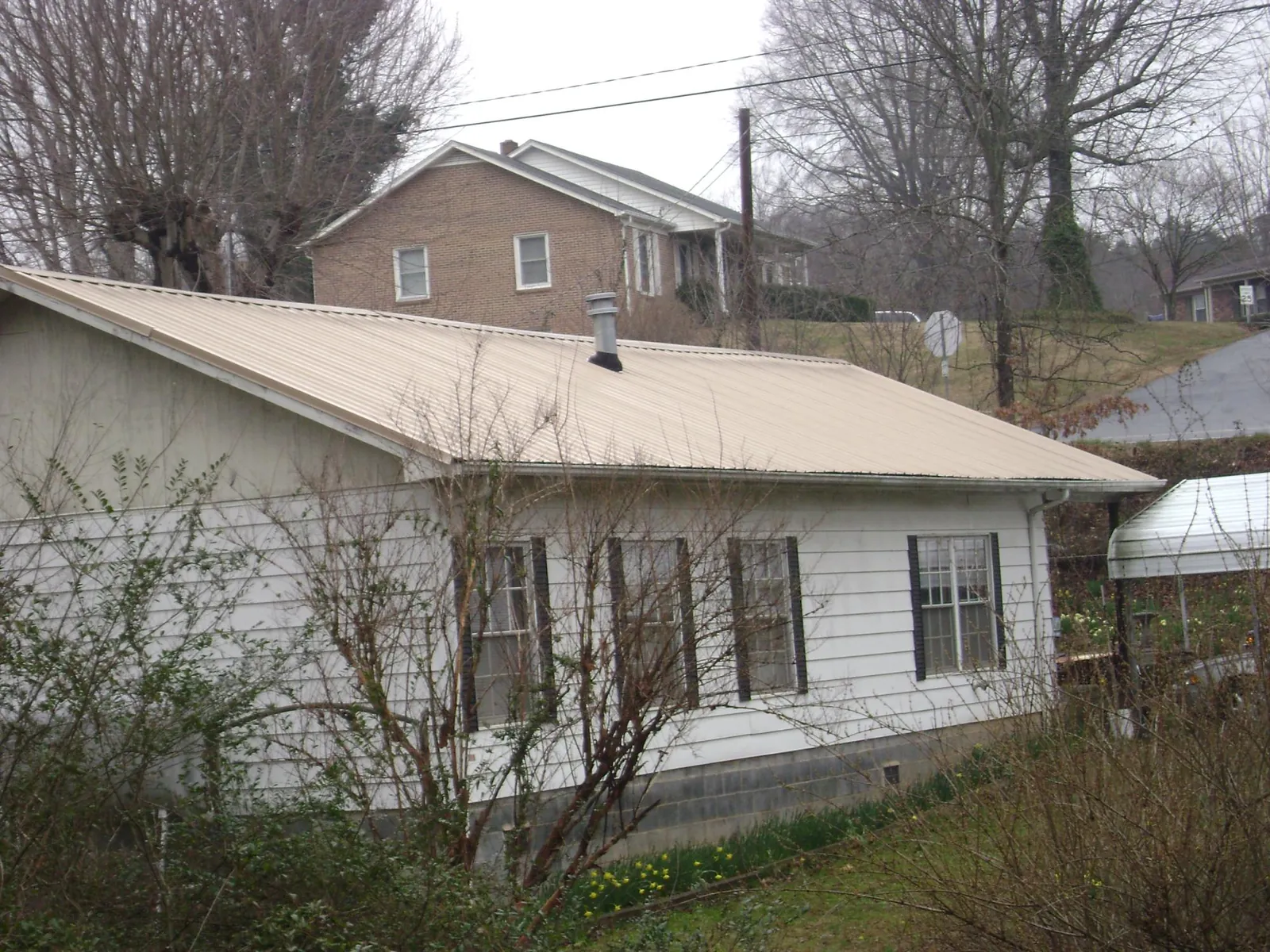 Tan metal roof on a white sided house set into a hillside — Commercial Roofing by Roofing Brothers in Clarkson