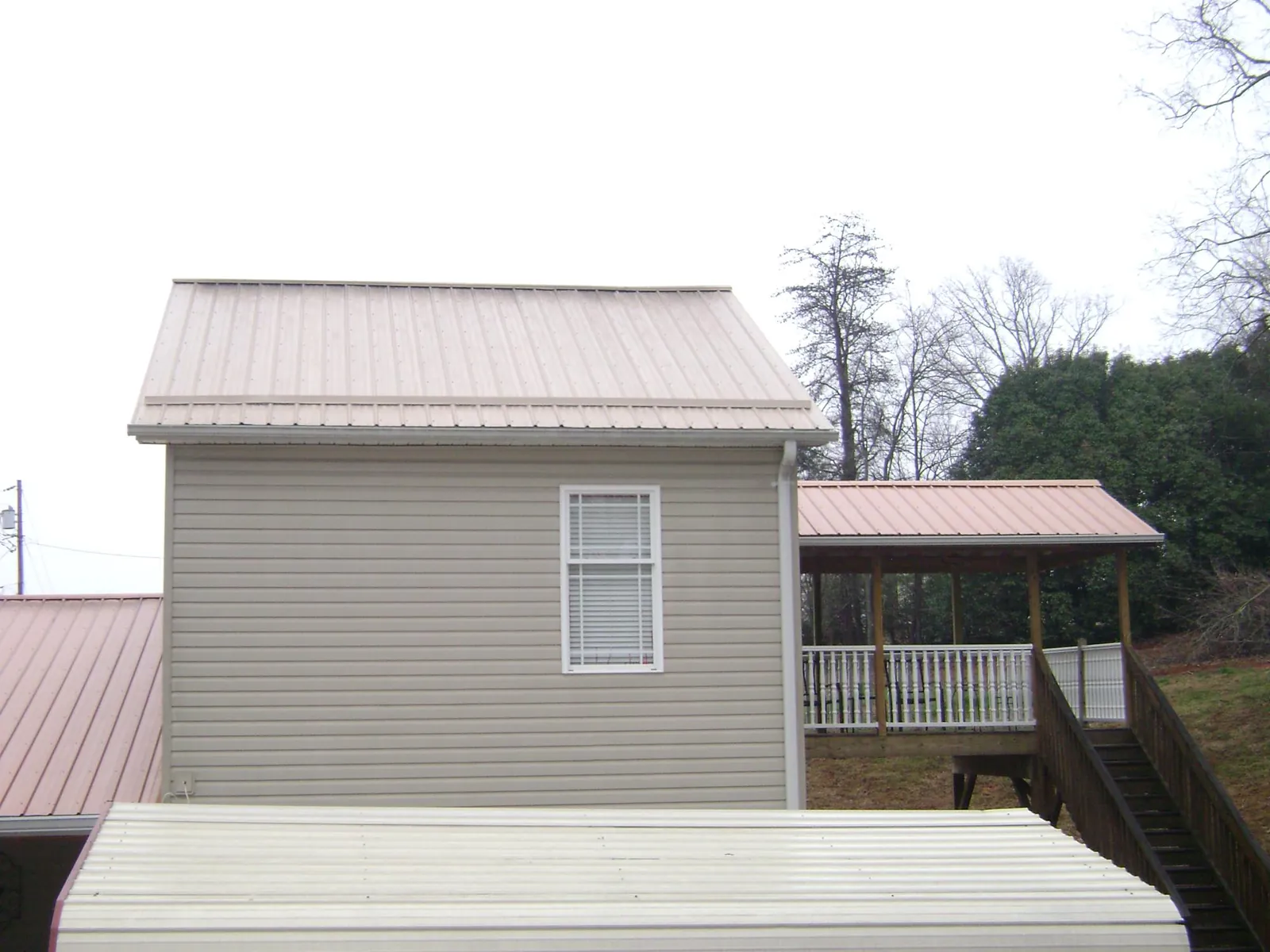 Tan metal roofs on a two story addition and attached porch, from a Roof Replacement job in Clarkson
